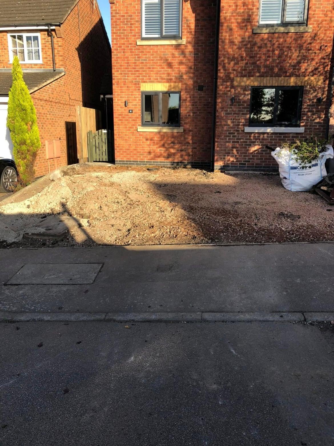 Front of a red brick house with the old driveway excavated ready for a new base