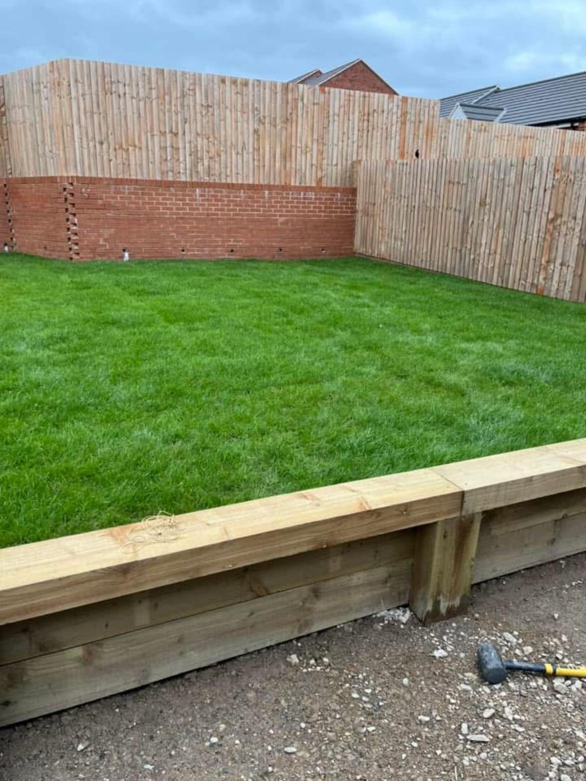 Freshly laid turf behind a raised timber sleeper edge, with new feather-edge fencing