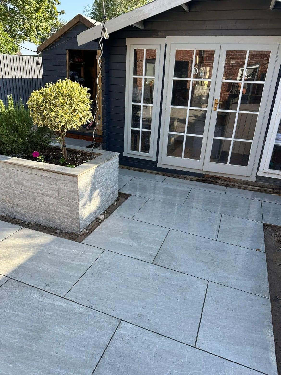 Grey porcelain paving meeting a clad raised planter beside a summerhouse