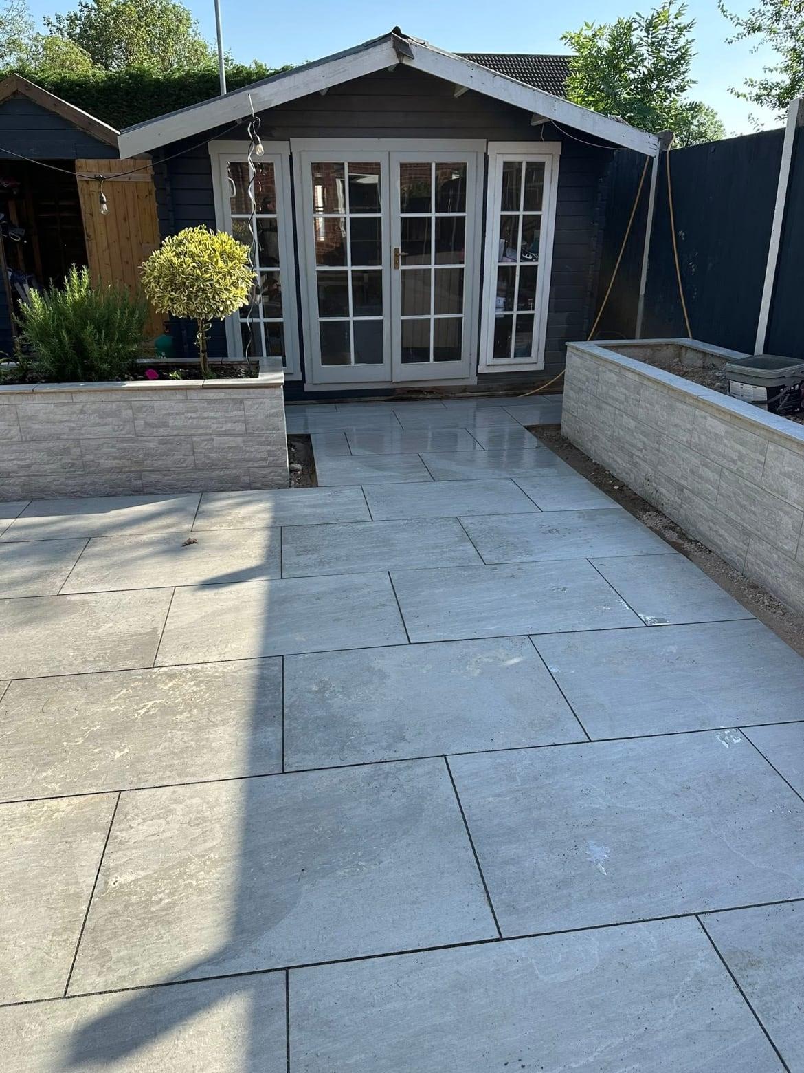 Large-format grey porcelain patio leading to a painted summerhouse, with clad raised planters on both sides