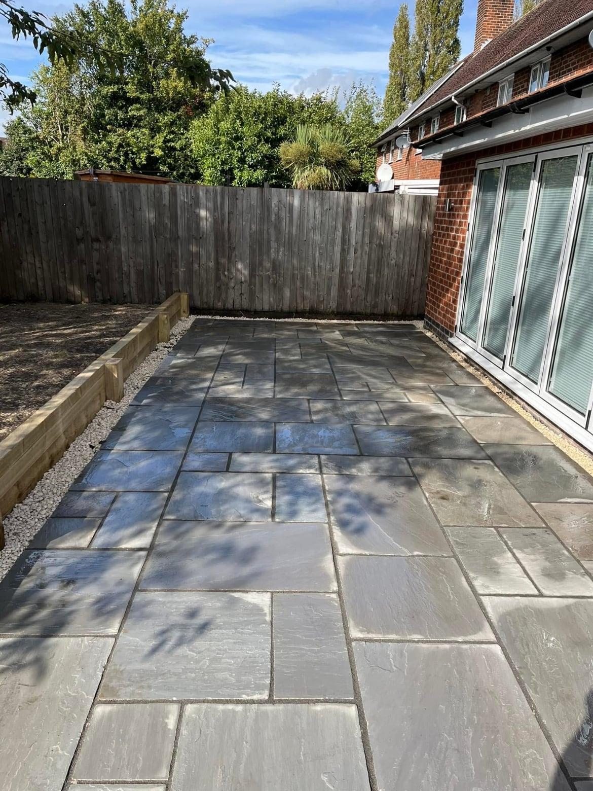 Grey sandstone patio laid outside bi-fold doors with timber sleeper edging along the boundary