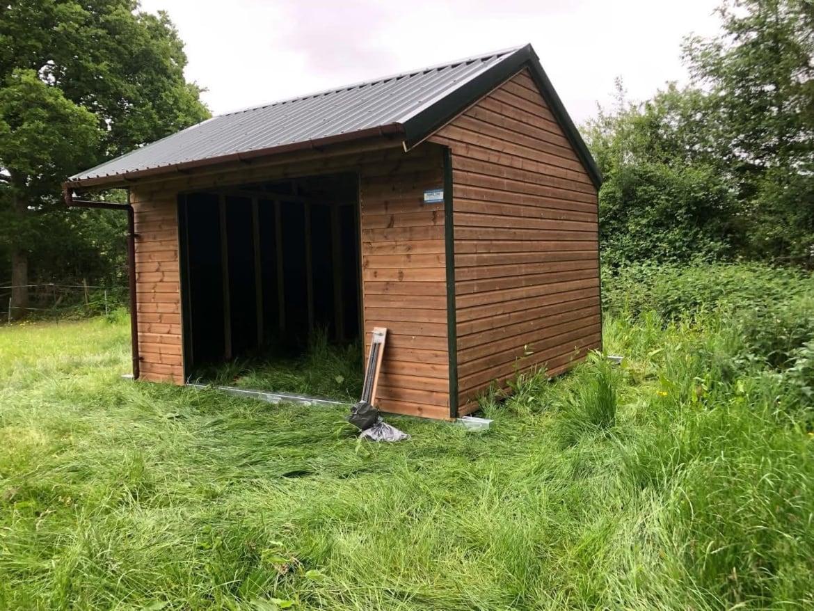 Open-fronted timber field shelter with a dark metal roof in a grass paddock